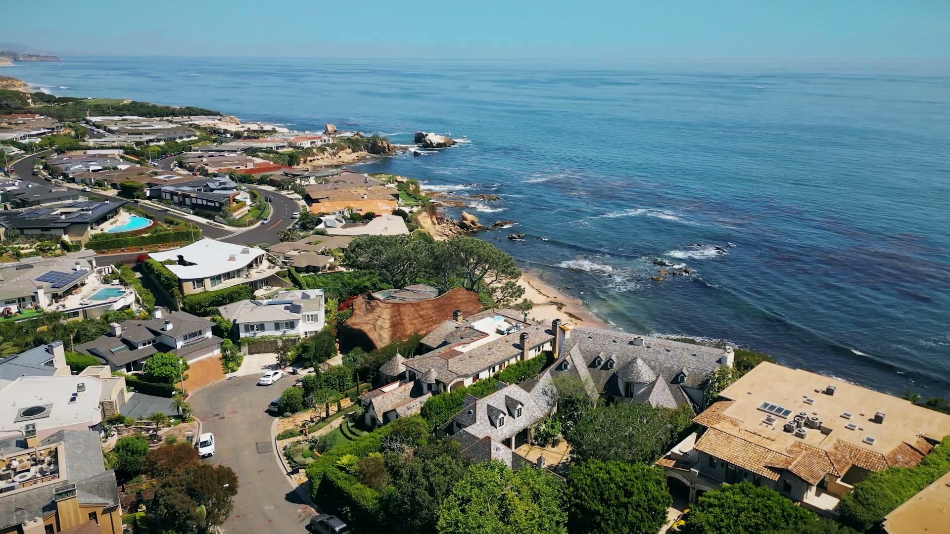 Aerial view of houses along a bluff above a rocky shoreline and the open ocean