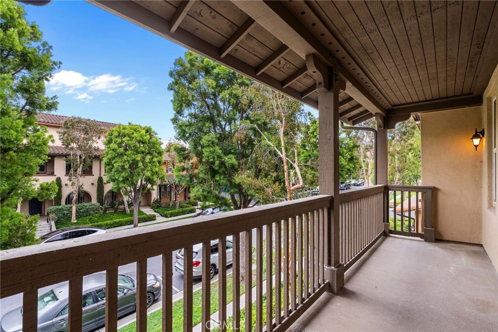 A covered balcony with a wood railing above a tree-lined street